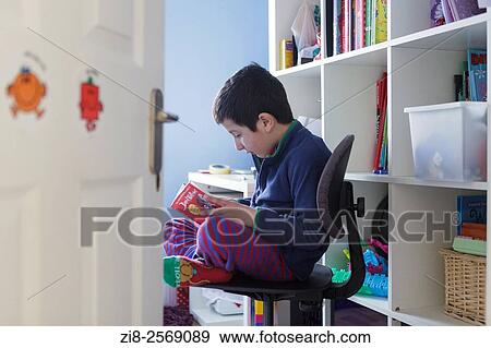 Stock Photo - Schoolboy, 6 years ol, reading a book in his room.. Fotosearch