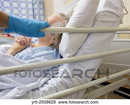 Son at bedside of 90 year old Mother wears gloves as part of infection control in National Health Service Hospital in England, United Kingdom. View Large Photo Image Stock Photo - Son at bedside of 90 year old Mother wears gloves as part of infection control in National Health Service Hospital in England, United Kingdom.. Fotosearch