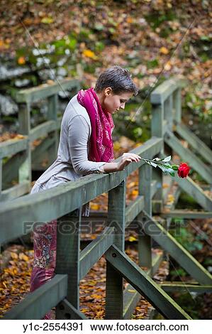 Stock Photo - Lonesome young lady with rose flower in hand View Large Photo Image Stock Image - Stock Photo - Lonesome young lady with rose flower in hand. Fotosearch
