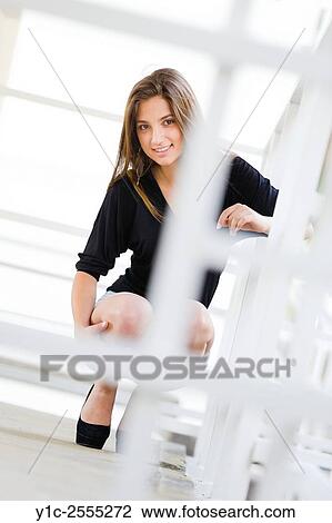 Stock Image - Stock Photo - Teen girl is squatting smiling behind White metal fence. Fotosearch