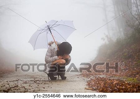 Stock Photograph - Stock Photo - Young woman squatting under umbrella alone and lost. Fotosearch
