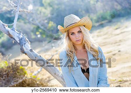 Stock Image - Stunning blonde countrygirl in denim shirt before tree. Fotosearch