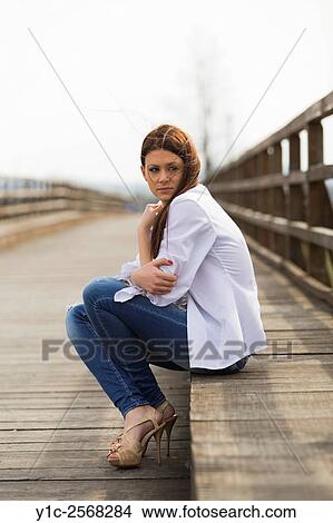 Picture - Teenager girl is cold sitting on bridge waiting looking back. Fotosearch