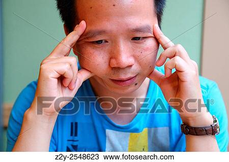 Stock Image - Thinking chinese young man with hands on the lateral of his face.. Fotosearch