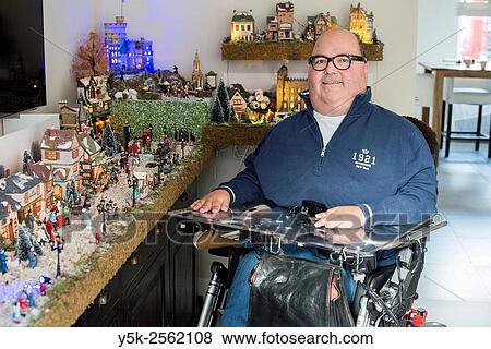 Stock Photo - Tilburg, Netherlands. Disabled man in wheelchair due to muscular distrophy posing at home in front of his Dickens Christmas village.. Fotosearch