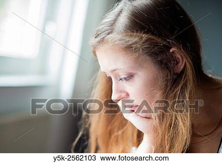 Stock Image - Tilburg, Netherlands. Young woman with her head leaning on her hand, while reading from her desk.. Fotosearch