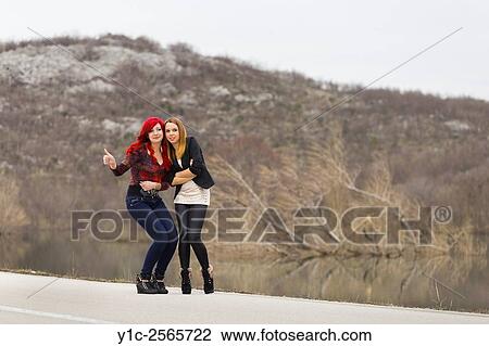Stock Image - Two teen girls are hitch hiking, thumb up. Fotosearch