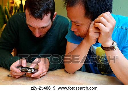 Stock Photo - Two young man looking at the display of a digital camera.. Fotosearch