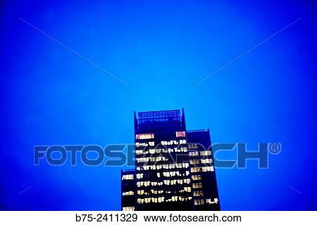 Stock Photo - View of the top of an office building with windows with the lights on in the evening and with a very blue sky in Canary Wharf, London, England, UK, Europe.. Fotosearch