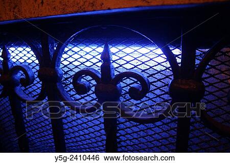 Stock Photograph - Window with blue neon light and wrought iron fittings and grill at night. Fotosearch