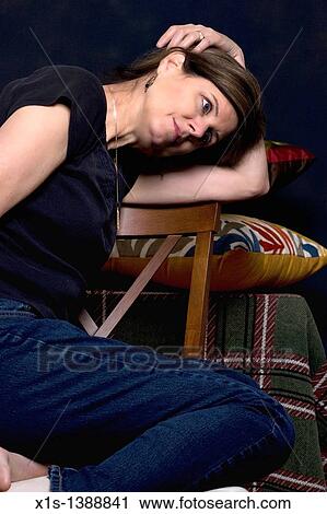 Woman in black shirt and dark jeans sits sideways on a high back chair with her head resting on one arm and her hand draped over her head, looking off. View Large Photo Image Stock Image - Woman in black shirt and dark jeans sits sideways on a high back chair with her head resting on one arm and her hand draped over her head, looking off.. Fotosearch