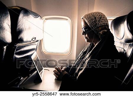 Stock Photo - Woman watching movie on tablet device in window seat on airplane.. Fotosearch