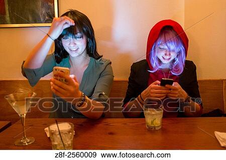 Stock Photo - Women wearing wigs checking their phones at a bar in New York City, New York, USA.. Fotosearch