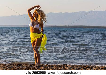 Stock Photograph - Young blonde woman on beach in sunset.. Fotosearch