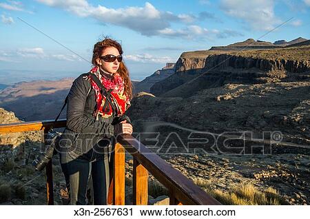 Stock Image - Young woman leaning agains a railing gazing at the landscape over Sani Pass, Lesotho, Africa.. Fotosearch