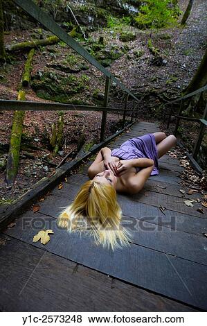 Stock Photo - Young woman lying on wooden footbridge with spread blond hair. Fotosearch