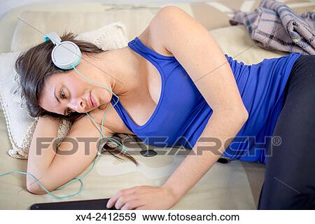 Stock Photo - Young Woman relaxing on her sofa and listening to music on her tablet with Headphones.. Fotosearch