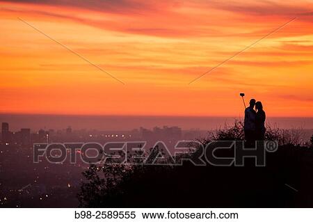 A couple using a selfie stick at sunset in Griffith Park in the Hollywood Hills overlooking Los Angeles. View Large Photo Image Stock Photography - A couple using a selfie stick at sunset in Griffith Park in the Hollywood Hills overlooking Los Angeles.. Fotosearch