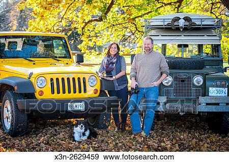 A man and woman standing in front of a Jeep Wrangler and a Land Rover with a border collie. View Large Photo Image Stock Photo - A man and woman standing in front of a Jeep Wrangler and a Land Rover with a border collie.. Fotosearch