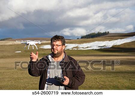 Stock Photo - A man flying a small drone catches it in the air.. Fotosearch