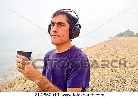 A man is listening music with his headphones while he is holding on a plastic glass of coffee. View Large Photo Image Stock Photo - A man is listening music with his headphones while he is holding on a plastic glass of coffee.. Fotosearch