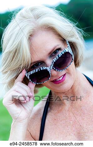 Stock Photo - A portrait of a 56 year old blond woman looking over her sunglasses directly at the camera, outdoors.. Fotosearch
