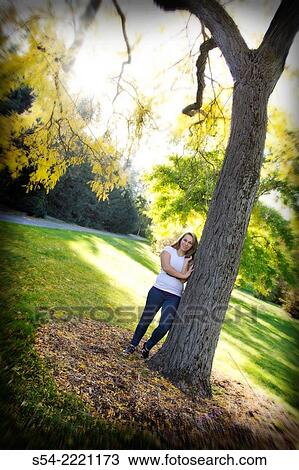 Stock Image - A teen girl leaning against a tree in a park.. Fotosearch