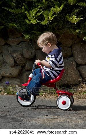 A young boy riding a red trike outdoors. View Large Photo Image Stock Photography - A young boy riding a red trike outdoors.. Fotosearch