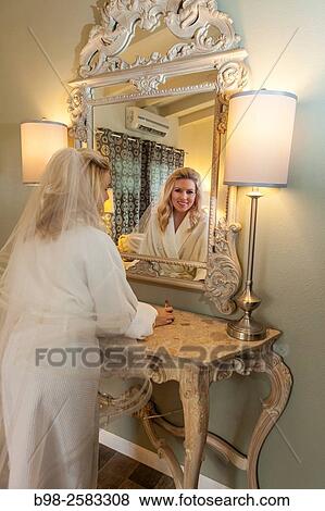 Stock Photo - A young bride Bride looking in a mirror getting ready for wedding.. Fotosearch