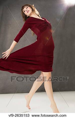 Attractive young woman dancer in long burgundy tango dress, turning with dress swirling, with light flare on gray background. View Large Photo Image Stock Image - Attractive young woman dancer in long burgundy tango dress, turning with dress swirling, with light flare on gray background.. Fotosearch