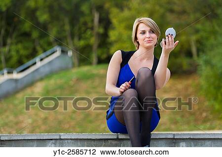 Stock Image - Attractive young woman fixing-up admiring herself in small mirror. Fotosearch