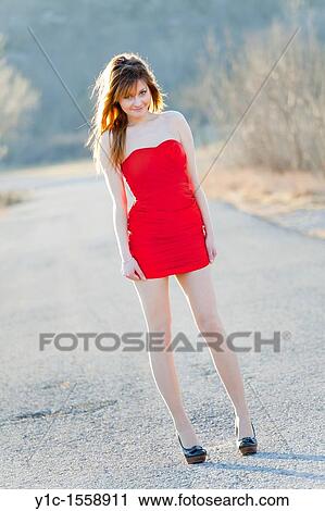 Stock Image - Attractive young woman is standing on the country-road and smiling. Fotosearch