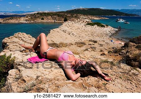 Stock Photo - Attractive young woman sunbathing atop stone. Fotosearch