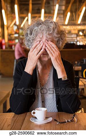 Beautiful senior woman, with grey hair, hiding her eyes in sign of depression, elbows resting on table, in a cafe, with a cup of coffee and her glasses in front of her View Large Photo Image Stock Image - Beautiful senior woman, with grey hair, hiding her eyes in sign of depression, elbows resting on table, in a cafe, with a cup of coffee and her glasses in front of her. Fotosearch