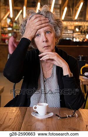 Beautiful senior woman, with grey hair, holding her forehead in sign of headache or depression, one elbow resting on the table, in a cafe, with a cup of coffee and her glasses in front of her View Large Photo Image Stock Image - Beautiful senior woman, with grey hair, holding her forehead in sign of headache or depression, one elbow resting on the table, in a cafe, with a cup of coffee and her glasses in front of her. Fotosearch