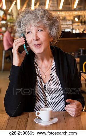 Beautiful senior woman, with grey hair, happy looking, using her i-phone and smiling, with a cup of coffee in front of her, in a cafe View Large Photo Image Stock Photography - Beautiful senior woman, with grey hair, happy looking, using her i-phone and smiling, with a cup of coffee in front of her, in a cafe. Fotosearch