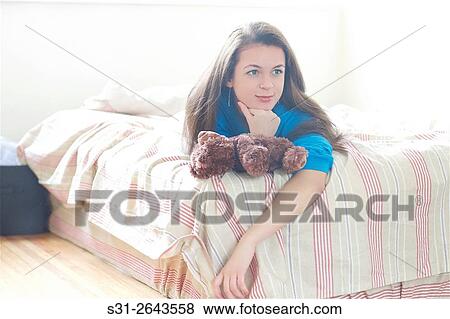 Stock Photo - beautiful young Russian girl on lying on bed with teddy bear.. Fotosearch
