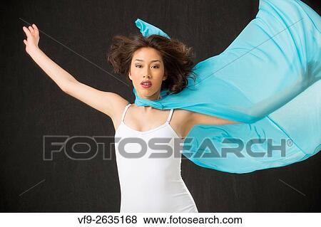 Stock Photo - Beautiful young woman dancer, half length in light blue cape and white leotard, reaching up with one arm covered in transparent, winglike fabric, against black background.. Fotosearch