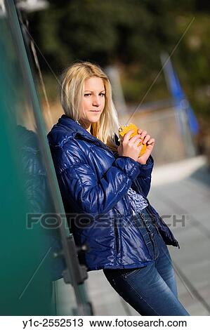 Stock Image - Blonde teenager girl eating sandwich outdoors. Fotosearch