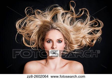 Picture - Blonde woman lying down with a letter X card covering her mouth.. Fotosearch