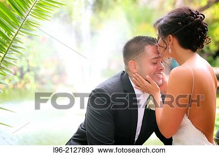 Stock Image - bride kissing groom on forehead in a garden setting with a fountain. Fotosearch