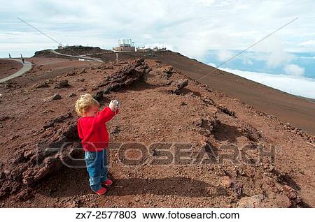 Stock Image - Child taken pictures in the Summit of Puu Ulaula. Maui. Hawaii. Summit of Puu Ulaula with departing several trekings foot or horseback to descend 900 meters into the bowels of the volcano ash filled paths. Haleakala Pu`u `Ula`ula Summit Hill.. Fotosearch