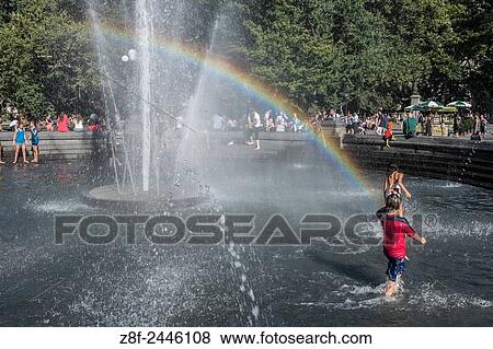 Stock Photo - Children play under a rainbow on a hot summer day in the fountain in Washington Square Park.. Fotosearch
