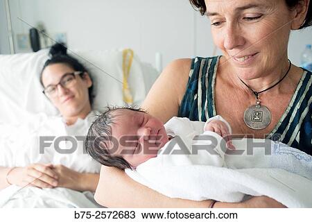Close up of a newborn baby in the arms of her grandmother and the mother in the background baby in bed. View Large Photo Image Stock Image - Close up of a newborn baby in the arms of her grandmother and the mother in the background baby in bed.. Fotosearch