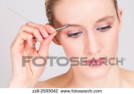 Stock Image - Close up of a young woman plucking her eyebrows.. Fotosearch