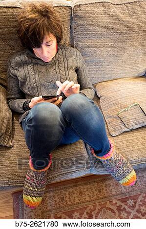 Stock Image - Closeup of a woman sitting on fitness informal and relaxed on a couch, manipulating a cell phone. Buckden, Skipton, Yorkshire Dales, England, UK, Europe. Fotosearch