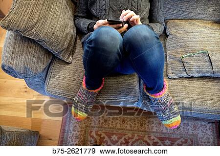 Stock Photo - Closeup of a woman sitting on fitness casual and relaxed on a couch, manipulating a cell phone. Buckden, Skipton, Yorkshire Dales, England, UK, europe. Fotosearch