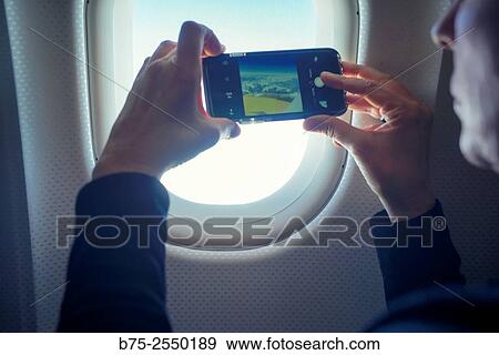Closeup of hands of a young woman taking a picture with a mobile phone, -through a window in an airplane View Large Photo Image Stock Photo - Closeup of hands of a young woman taking a picture with a mobile phone, -through a window in an airplane. Fotosearch