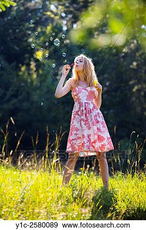 Stock Photo - Country-girl blowing bubbles in nature on grass-field. Fotosearch