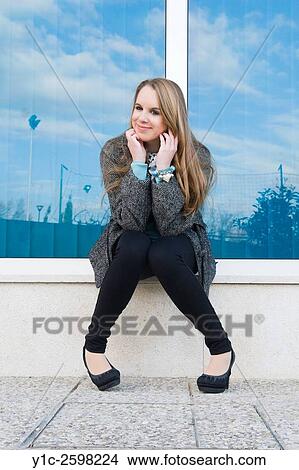 Picture - Cute teen-girl sitting and waiting before shiny glass wall. Fotosearch